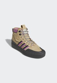 Beige höga sneakers med lila och svarta ränder, texturerad suede ovandel, silverfärgade snören och gummiklädd sula med räfflat mönster.