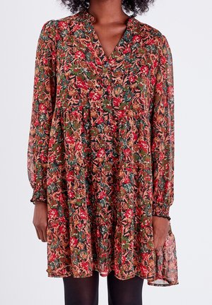 Woman wearing a long-sleeve, floral button-up dress with elastic cuffs and a flared hem in red, green, and brown tones.