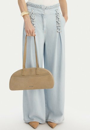 Light blue wide-leg jeans with lace-up details, beige suede handbag, gold cuff bracelet, and pointed beige shoes on a person.