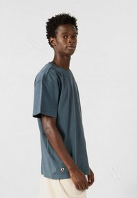 T-shirt a maniche corte, collo rotondo, in cotone blu scuro, con un logo discreto sull'orlo, vestibilità rilassata e texture liscia.