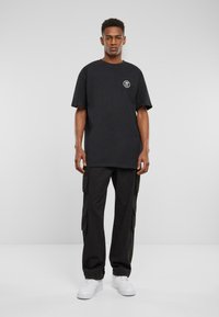 Black oversized t-shirt with short sleeves and a round neckline, featuring a small logo on the left chest. Paired with black cargo pants.