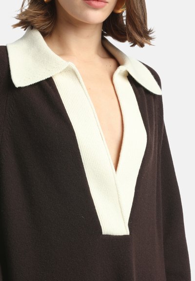 Hnedý pletený sveter s krémovým rebrovaným golierom, s hlbokým výstrihom do V a uvoľneným strihom. Textúrovaná tkanina s kontrastnými farbami.