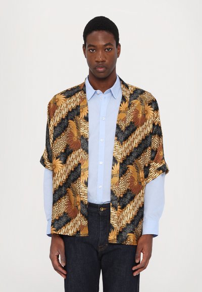 Kortærmet kimono-stil skjorte med sort bund, guld- og brune blomsterprint, parret med en lyseblå skjorte med knapper og mørke jeans.