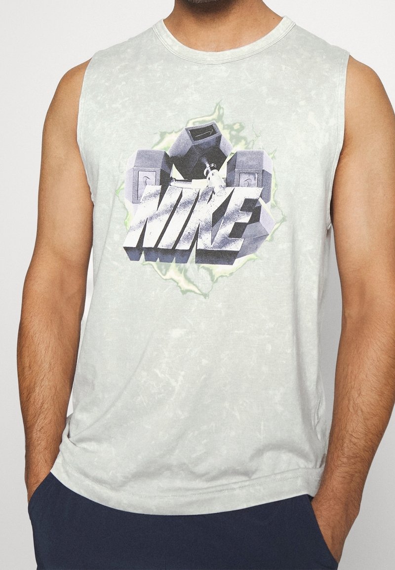 Débardeur gris clair avec un logo Nike audacieux. Le tissu présente une texture délavée avec une coupe douce et décontractée.