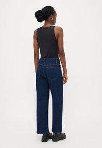 Jeans de denim escuros, folgados, com cintura alta e dois bolsos traseiros, combinados com uma blusa preta sem mangas. Textura suave.