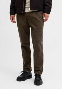 Bruna skräddarsydda byxor i textil, med rak passform och frontveck, tillsammans med svarta snörskor.