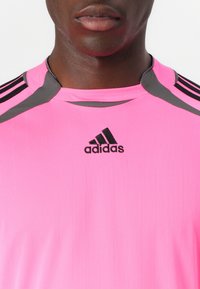 Pink sports shirt with vertical lines. Features black Adidas logo and gray accents on shoulders. Made of lightweight fabric.