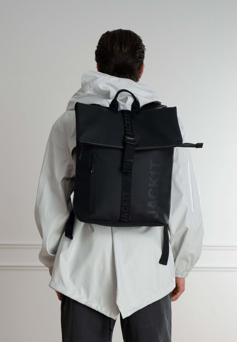 Zaino roll-top nero con finitura opaca, dotato di una tasca anteriore con zip e spallacci regolabili. Logo stampato sul lato.