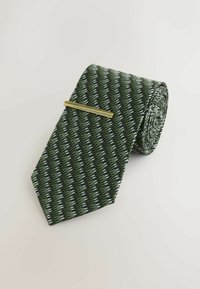 Green patterned tie with diagonal stripes in dark and light shades, featuring a gold tie clip. Made of textured fabric, rolled neatly.