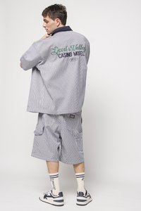 Striped short-sleeve shirt and cargo shorts in blue and white, featuring "Devil's Valley Casino Motel" embroidery on the back. Sneakers and socks visible.