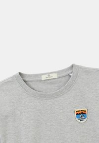 T-shirt en coton gris avec un col rond, arborant un patch brodé qui affiche "PLAY TEAM COLORADO 1992" en bleu, orange et jaune.