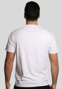 T-shirt bianca in cotone a maniche corte, collo rotondo e design posteriore semplice. Texture morbida, vestibilità standard. Nessun motivo o accento visibile.