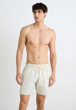 Shorts de bain beige avec une taille élastique et un cordon de serrage, présentant des poches latérales et un tissu léger et texturé.