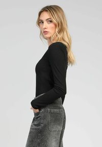 Haut noir à manches longues associé à une jupe en denim grise. Le haut présente une coupe ajustée, tandis que la jupe a un motif texturé et des poches.