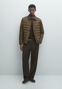 Brun quiltet jakke med krave, parret med en brun sweater og vide bukser. Mørke sko fuldender outfittet.