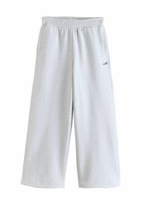 Pantaloni della tuta larghi grigio chiaro con cintura elastica e tasche laterali, caratterizzati da una piccola scritta "self." sulla coscia sinistra.