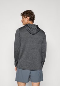 Haut à capuche gris à manches longues avec un tissu texturé, présentant une coupe ajustée et une couture dans le dos, associé à un short gris.