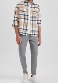 Koszula na guziki w beżowo-biało-niebieską kratę. Długie rękawy, dwa kieszenie z przodu. Połączona z szarymi, dopasowanymi spodniami i białymi trampkami.