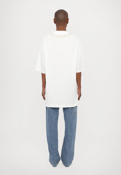 White oversized t-shirt with a round neckline, featuring a multicolored pattern around the collar. Paired with light-wash wide-leg jeans.