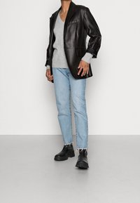 Schwarze Lederblazer, grauer V-Ausschnitt-Pullover, hellblaue Jeans mit fransigem Saum und klobige schwarze Stiefel. Schlichtes Design mit taillierter Silhouette.