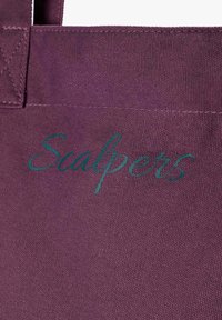 Bolsa de tela morada con el texto "Scalpers" en script color teal. El material tiene una apariencia texturizada con costuras resistentes.