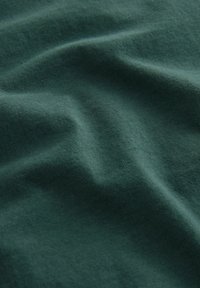 Mørkegrøn bomuldsstof med en glat tekstur, der har subtile folder og rynker, hvilket antyder fleksibilitet og blødhed.