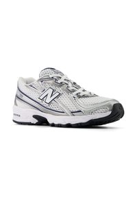 Sneaker sportiv gri și alb cu partea superioară din plasă, închidere cu șireturi și talpă din cauciuc. Caracteristici: logo-ul "N", detalii texturate și tehnologie de amortizare.