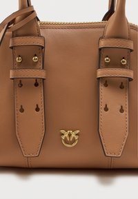 Τσάντα χρώματος ταμπά από δέρμα με δύο επίπελους χειρολαβές, χρυσά αξεσουάρ, διακοσμητική ραφή και ένα έμβλημα με δύο πουλιά και έναν δακτύλιο.