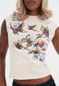 Camiseta corta beige con estampados coloridos de mariposas y flores, con sombreado detallado; cuello redondo y diseño sin mangas.