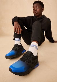 Zwart-blauwe sportschoenen met een verloopontwerp, mesh panelen en een zichtbare luchtkusseneenheid. Draagt witte sokken met strepen.