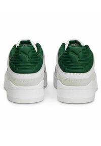 White sneakers with green padded heels, smooth and textured materials, thick soles, and subtle logo detailing on the heels.