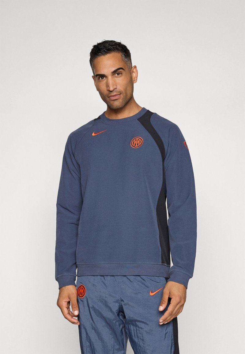 Felpa Nike in blu navy con dettagli arancioni. Caratterizzata da collo rotondo, maniche lunghe e pannelli laterali. Logo prominente sul petto.