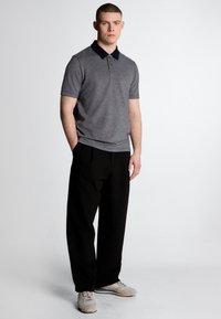 Grijze polo met een marineblauwe kraag, korte mouwen en een gestructureerde stof. Gecombineerd met zwarte broek en lichtgrijze sneakers.