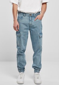 Lyseblå denim cargo bukser med elastiske manchetter, flere sidelommer og en afslappet pasform. Bæret med hvide sneakers og en enkel hvid skjorte.