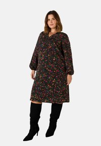 Šaty s květinovým potiskem z tmavé tkaniny s dlouhými balónovými rukávy a výstřihem do V. Obsahují živé barvy a volný, uvolněný střih. Nosené s černými kozačkami nad kolena.