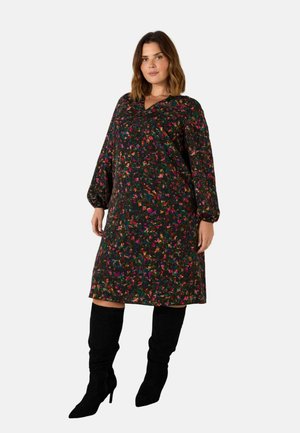 Bloemenprint jurk in donkere stof met lange ballonmouwen en een V-hals. Beschikt over levendige kleuren en een losse, ontspannen pasvorm. Gemaakt met zwarte kniehoge laarzen.