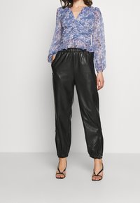 Blå gennemsigtig bluse med blomsterprint og lange ærmer med indsamlet detalje, kombineret med sorte læderjoggers med elastiske manchetter og sidelommer med lynlås.