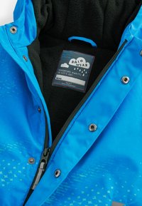 Veste de pluie bleu vif avec une doublure en polaire noire douce, dotée d'une fermeture éclair à l'avant, de fermetures à pression et d'un extérieur à motifs. Étiquetée "VÊTEMENTS DE PLUIE".