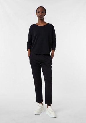 Black knit sweater with three-quarter sleeves, paired with black tapered pants and white sneakers. Simple design and smooth texture.