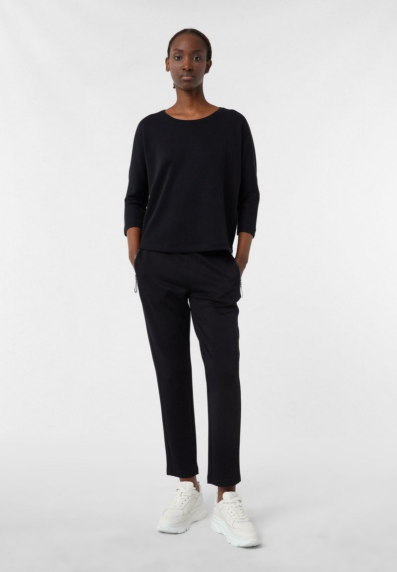 Pull en tricot noir à manches trois-quarts, associé à un pantalon noir fuselé et des baskets blanches. Design simple et texture lisse.