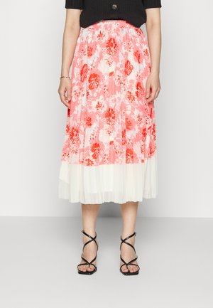 Saia midi plissada em rosa com padrão floral vermelho e saia interior branca; combinada com sandálias pretas de tiras. Os materiais e texturas variam.