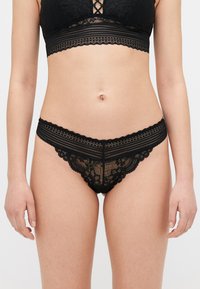 Svart blonde undertøy set med en bralette med blomsterdesign og en matchende truse. Begge har scallopkanter og myke teksturer.