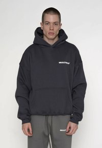 Hanorac gri închis cu buzunar frontal, glugă mare și logo alb "MULTIPLY" pe piept. Materialul pare moale și texturat.