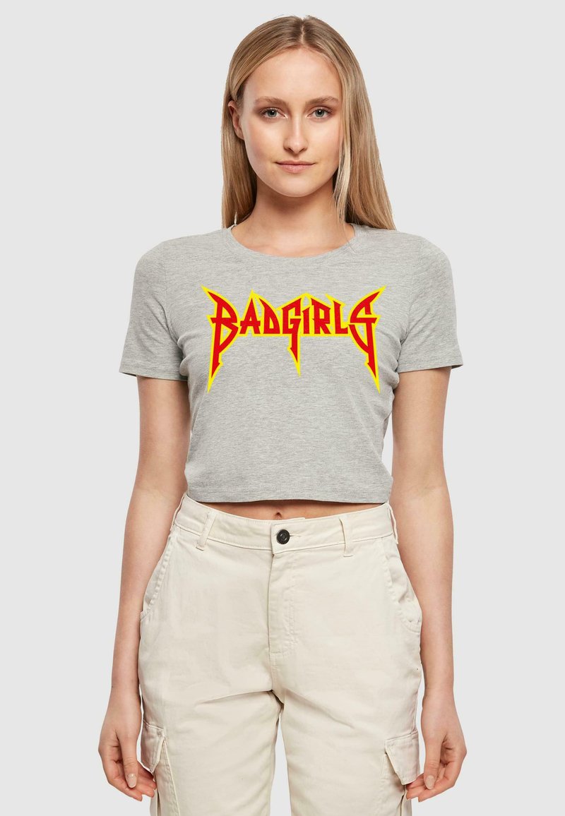 Pelēks īsa krekls ar "BADGIRLS" logo, kas izceltas bolder sarkanā un dzeltenā krāsā ar asiem, leņķainiem akcentiem. Gluda kokvilnas audums.