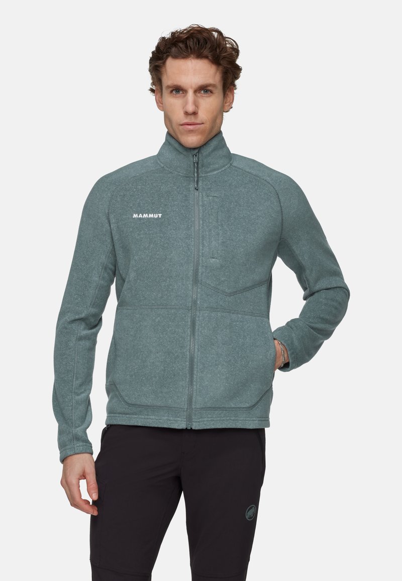 Giacca in pile di un verde teal tenue con colletto alto, zip integrale e tasca sul petto con zip. Presenta cuciture in contrasto e logo sul lato sinistro del petto.