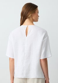 Blusa di lino bianca con apertura a chiave sulla parte posteriore, maniche corte e vestibilità comoda, con spacchi laterali per un maggiore comfort.