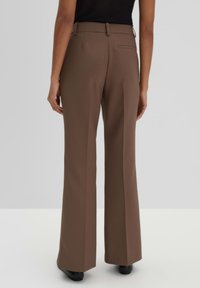 Pantaloni a zampa d'elefante marroni con una texture liscia, vita con passanti per cintura e una tasca posteriore singola. Progettati per una vestibilità su misura.