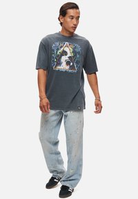 Grå grafisk t-shirt med en färgglad triangulär design, i kombination med ljusblå slitna jeans med färgspill och avslappnad passform.