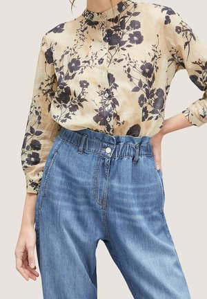 Beige bluse med lange ærmer og sorte blomsterprint, kombineret med lyseblå jeans med høj talje og elastisk linning.