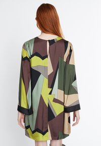 Robe à manches longues avec un motif géométrique en vert, beige et marron, dotée d'une fermeture à boutons au dos et d'une silhouette fluide.